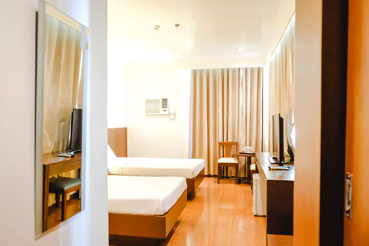 A hotel room with two beds, a desk, a chair, a TV, and a window with curtains.