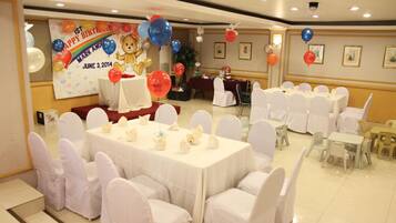 A banquet hall with round tables covered in white tablecloths and white chairs, decorated for a birthday event with balloons and a banner.