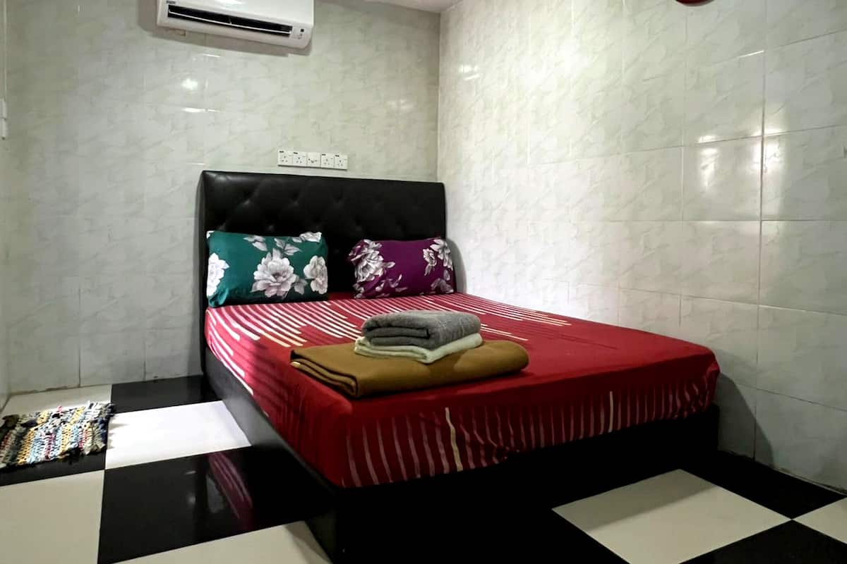 Una habitación de hotel con una cama, una colcha a rayas rojas y blancas, un suelo a cuadros negros y blancos y una unidad de aire acondicionado blanca en la pared.