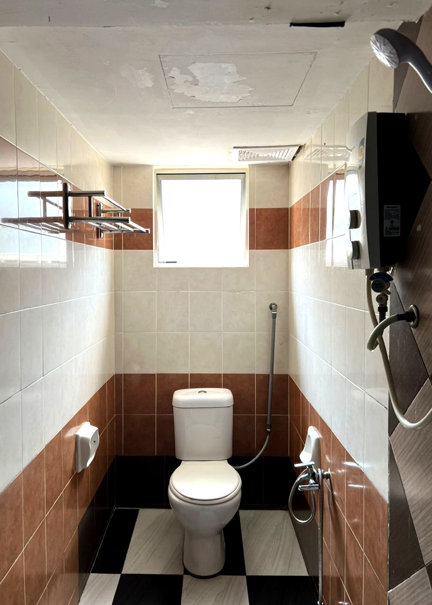 Et lille badeværelse med fliser, toilet, et vindue og en bruser.