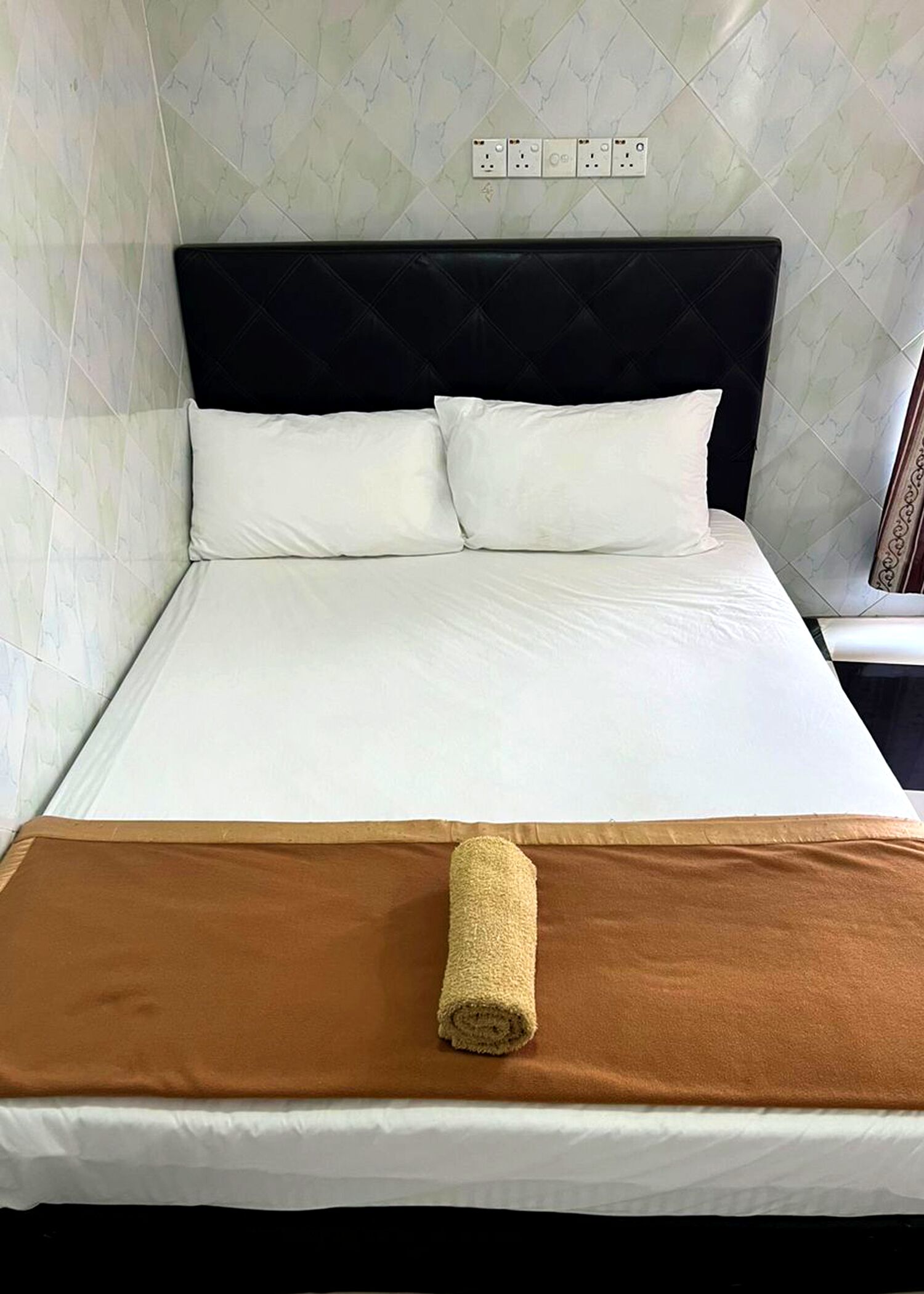 A neatly made bed with white linens, a brown throw blanket, and a rolled towel on the footboard.