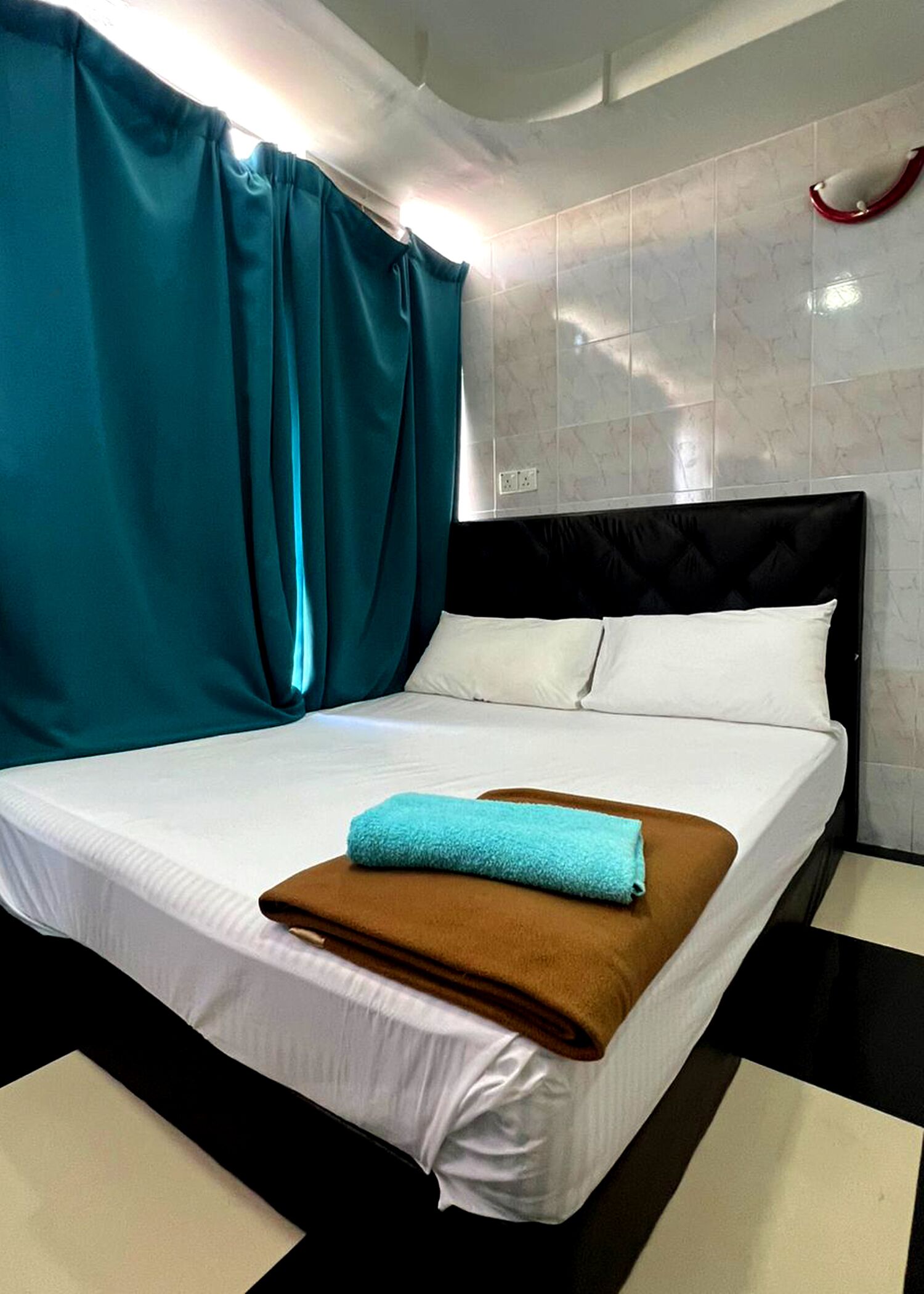 A neatly made bed with white and brown linens, teal curtains, and a red handle on the wall.