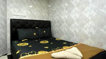 Una cama con cabecera negra y colcha marrón, almohada blanca y un adorno rojo en la pared.