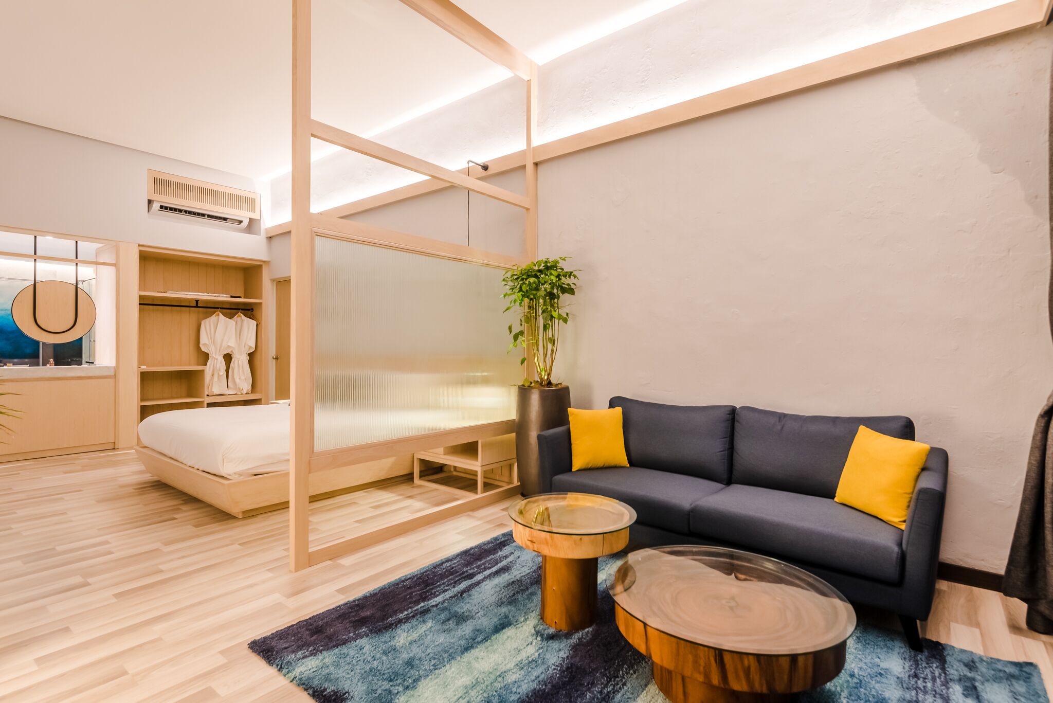A modern bedroom with a bed, bedside tables, a sofa, and a potted plant.