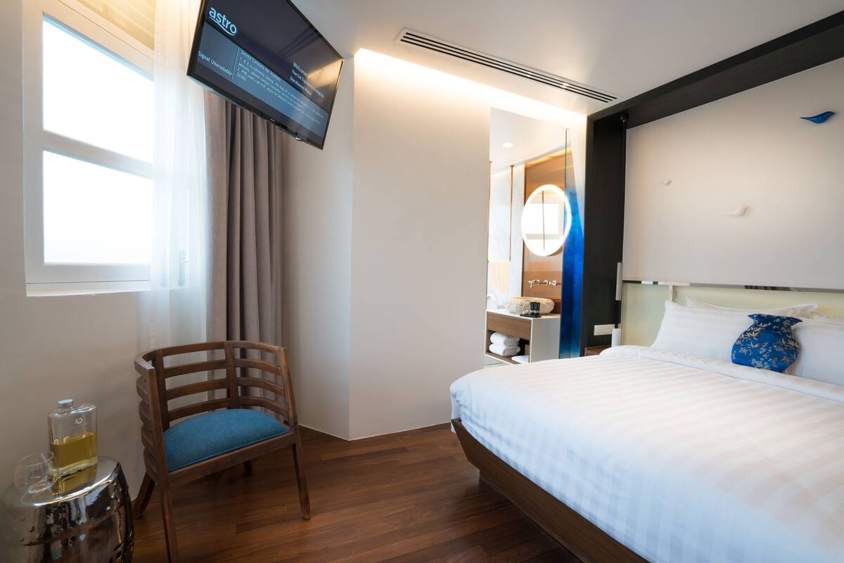 A hotel room with a bed, a chair, a TV, and a bathroom visible through an open door.
