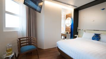 A hotel room with a bed, a chair, a TV, and a bathroom visible through an open door.