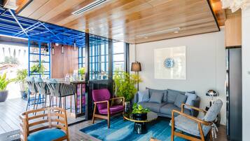 A modern living area with a wooden ceiling, blue accents, a sofa, chairs, a coffee table, and potted plants.