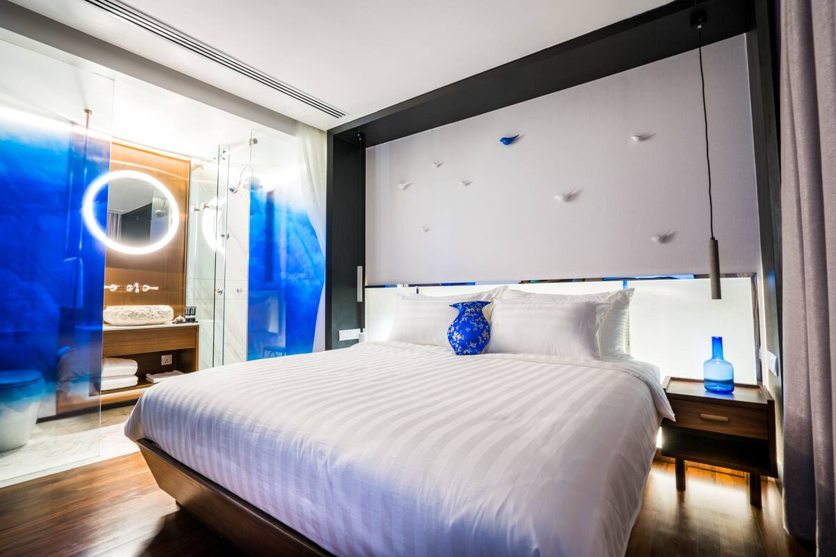 A modern bedroom with a large bed, a vanity with a mirror, and a blue vase on the nightstand.