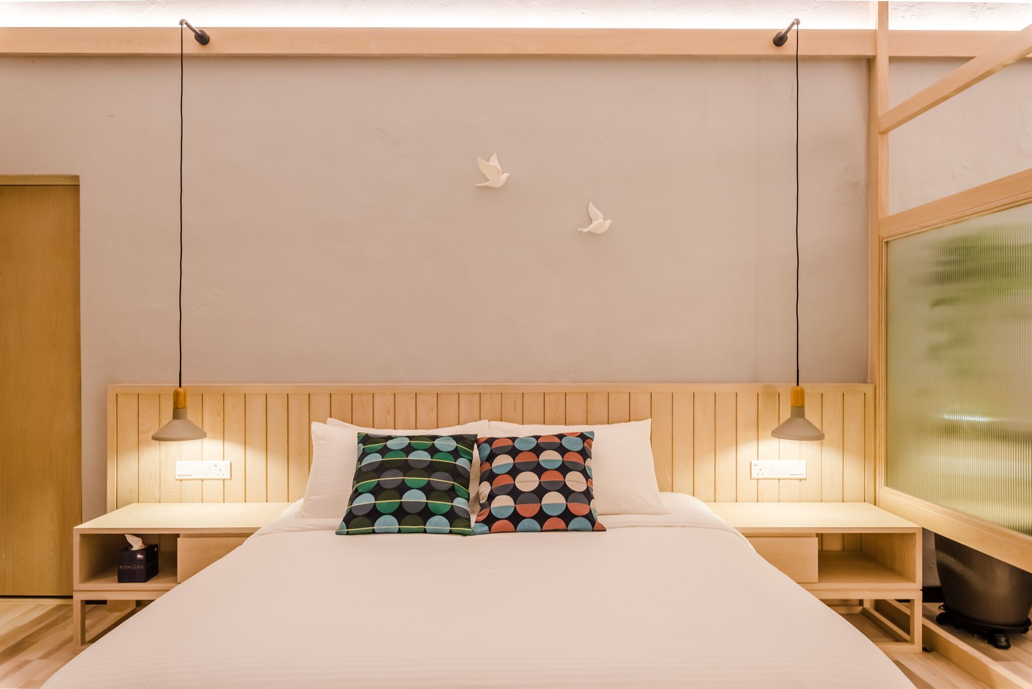 A hotel room with a wooden headboard, two bedside tables with lamps, a bed with white bedding, and two wall-mounted bird decorations.