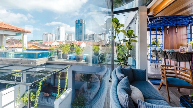 A modern rooftop terrace with a curved seating area, potted plants, and a view of the city skyline. - Tien Hotel (George Town)