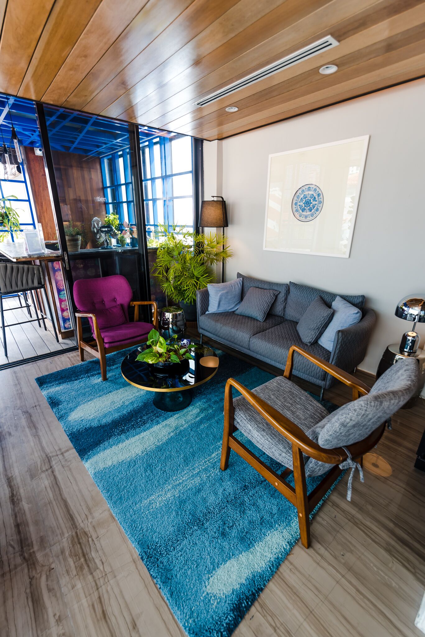 A modern living room with a blue rug, wooden furniture, a grey sofa, and a purple chair.