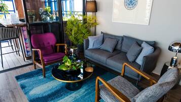 A modern living room with a blue rug, wooden furniture, a grey sofa, and a purple chair.