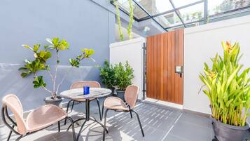 An outdoor patio with a round table and two wicker chairs, surrounded by potted plants and a wooden door.