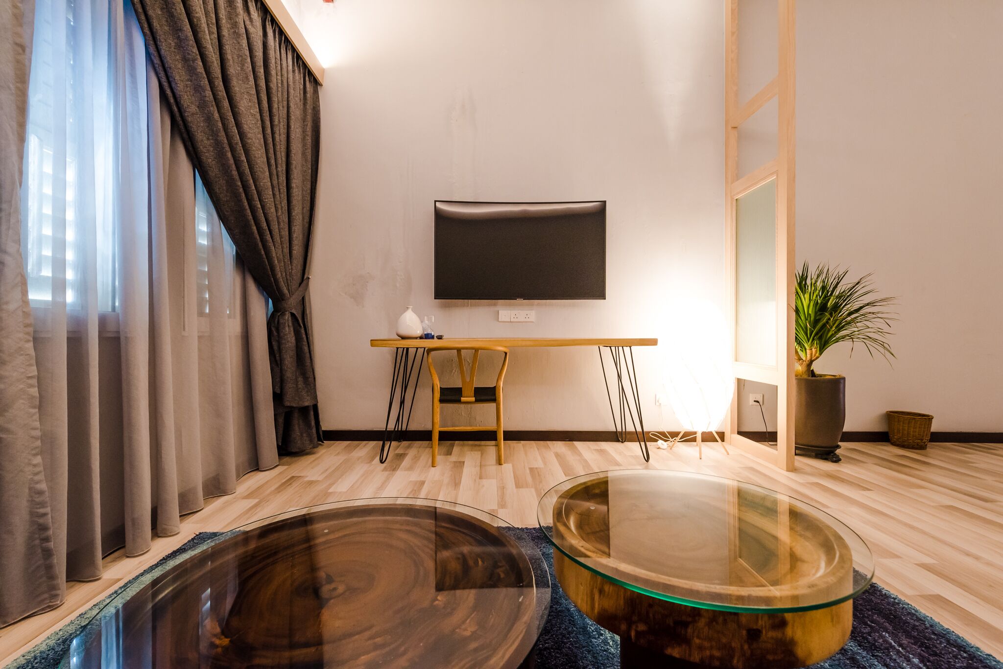 Una sala de estar moderna con un televisor de pantalla plana montado en la pared, una mesa de centro de madera y una mesa de vidrio con tapa de madera.