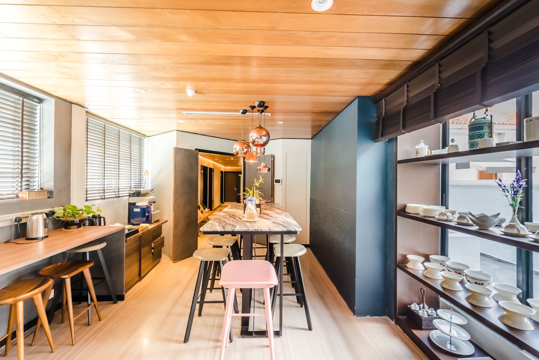 Une cuisine moderne avec un plan de travail en bois, des tabourets de bar, une table à manger avec des tabourets roses et un luminaire suspendu.