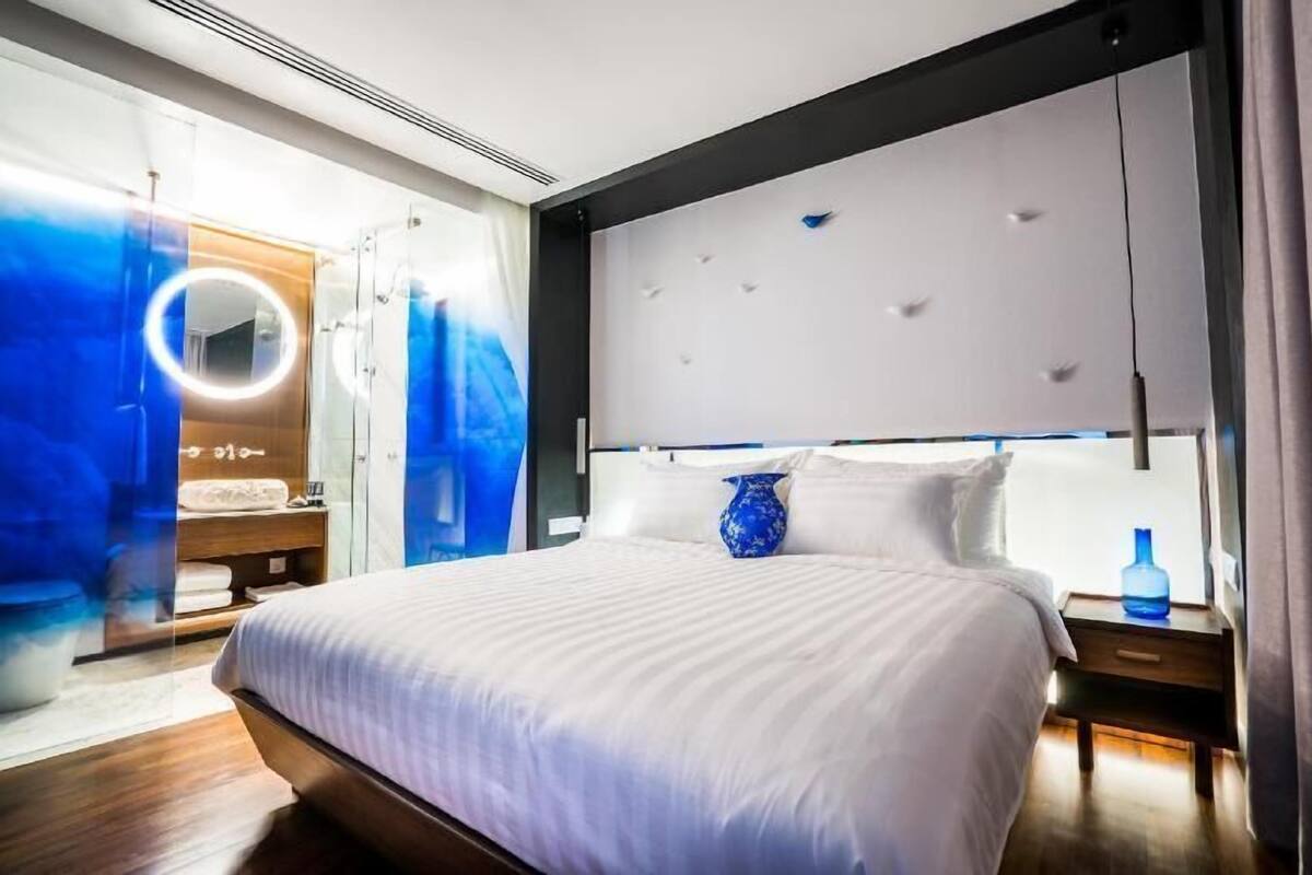 A modern hotel room with a large bed, a vanity with a mirror, and a blue vase on the nightstand.