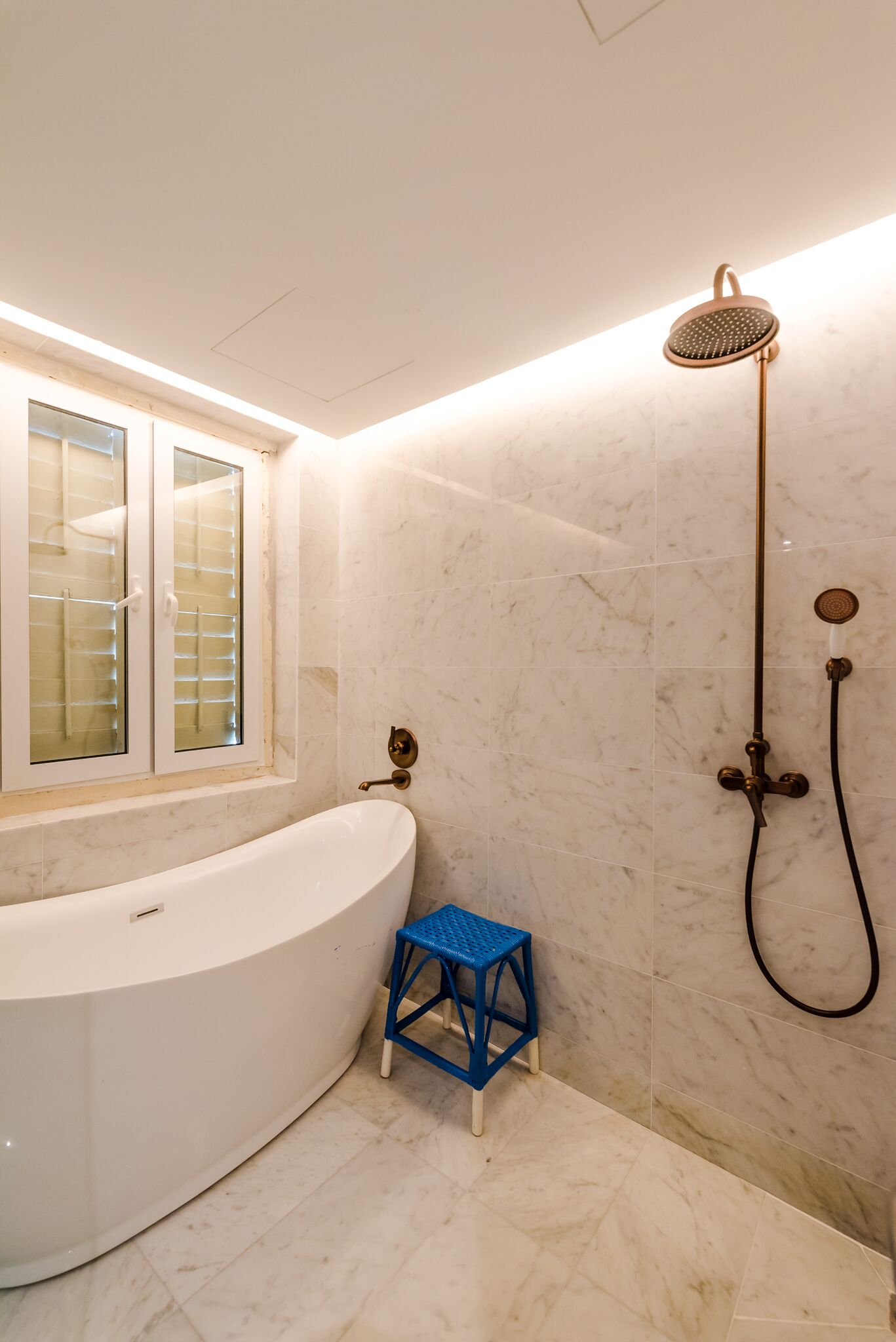 A bathroom with a white bathtub, a showerhead, and a small blue stool.