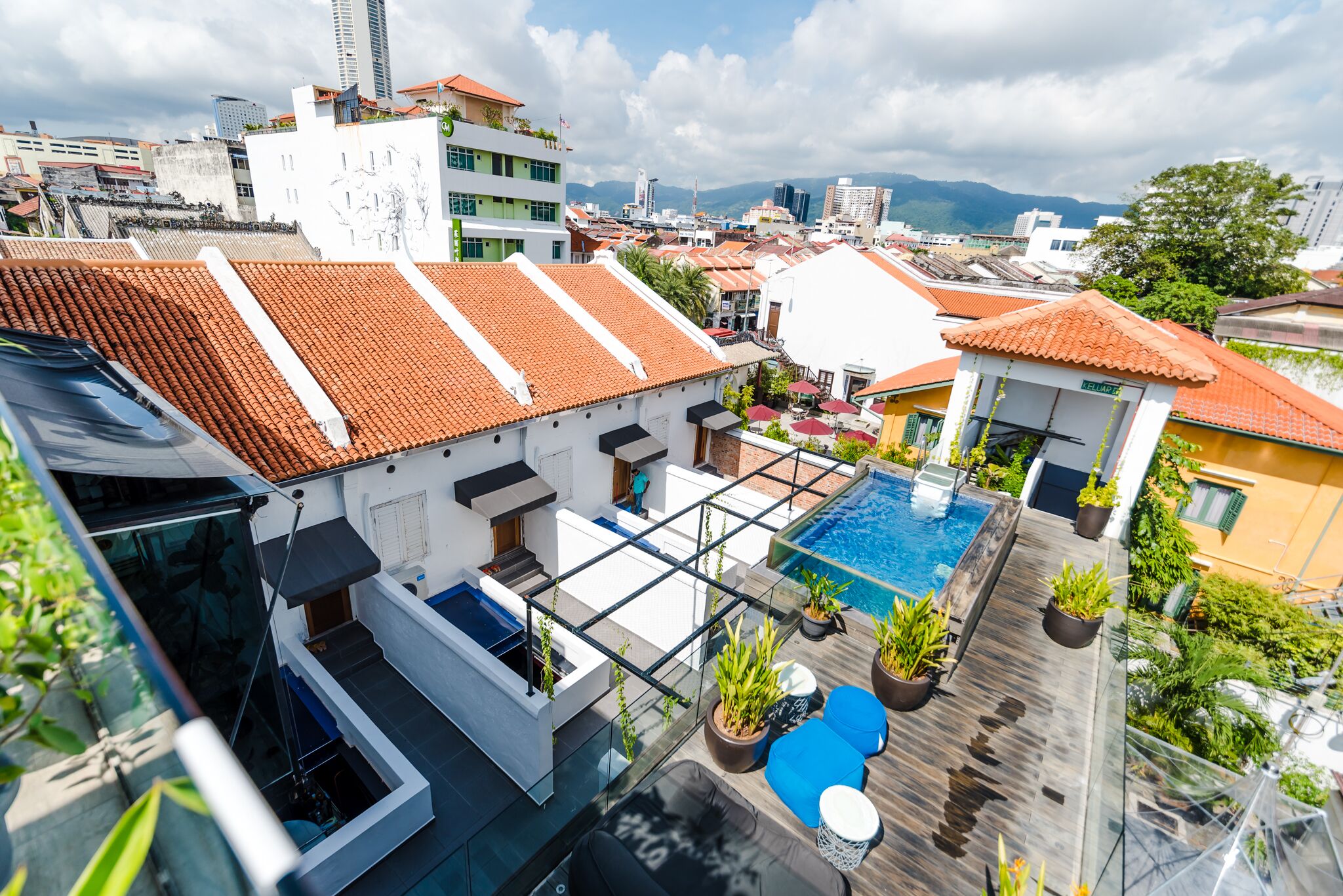 A rooftop pool area with a glass balustrade, potted plants, and outdoor seating.