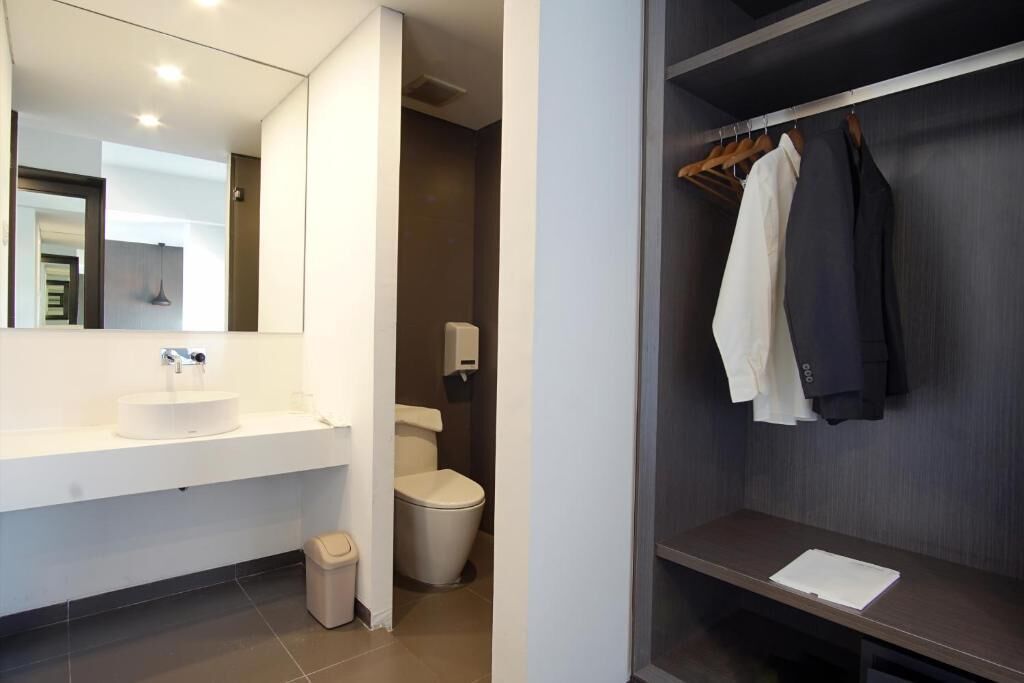Un baño moderno con un lavabo blanco, un inodoro y un espejo. Hay un cubo de basura pequeño y una repisa con un papel.
