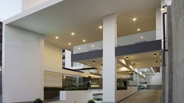 Un bâtiment moderne à plusieurs étages, doté de grandes fenêtres et d’un espace central ouvert avec un escalier.