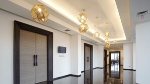 Un couloir d’hôtel moderne, avec un sol poli, des luminaires au plafond aux formes géométriques et des portes fermées.
