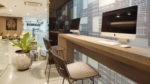 Un comptoir d’accueil moderne équipé de deux ordinateurs Apple iMac, d’une plante en pot et d’un espace détente avec des fauteuils.