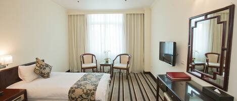Habitación de hotel con dos camas, un escritorio, una silla, un televisor y un espejo grande.