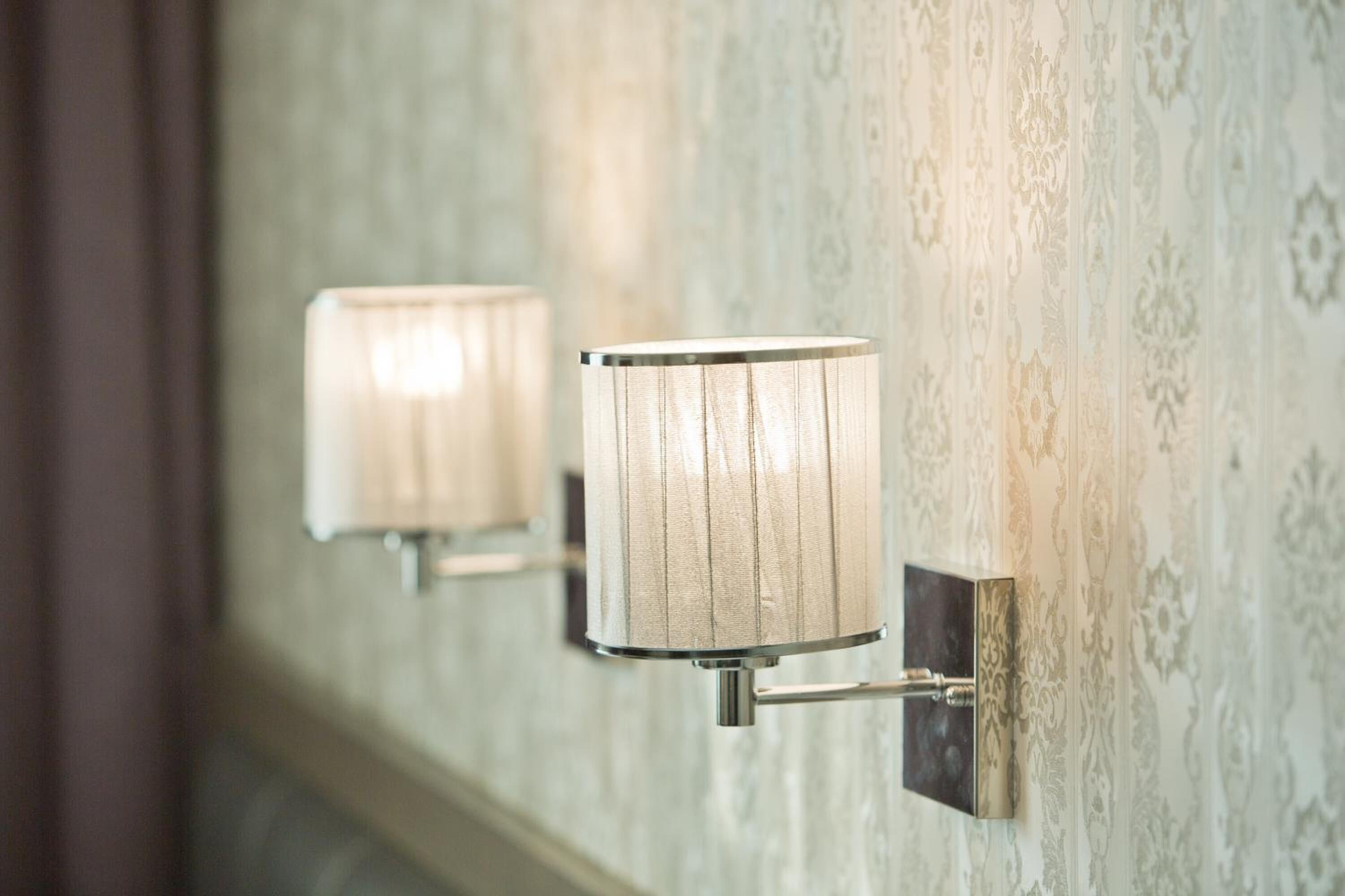 A wall-mounted light fixture with a cylindrical shade, mounted on a textured wall with a patterned design.