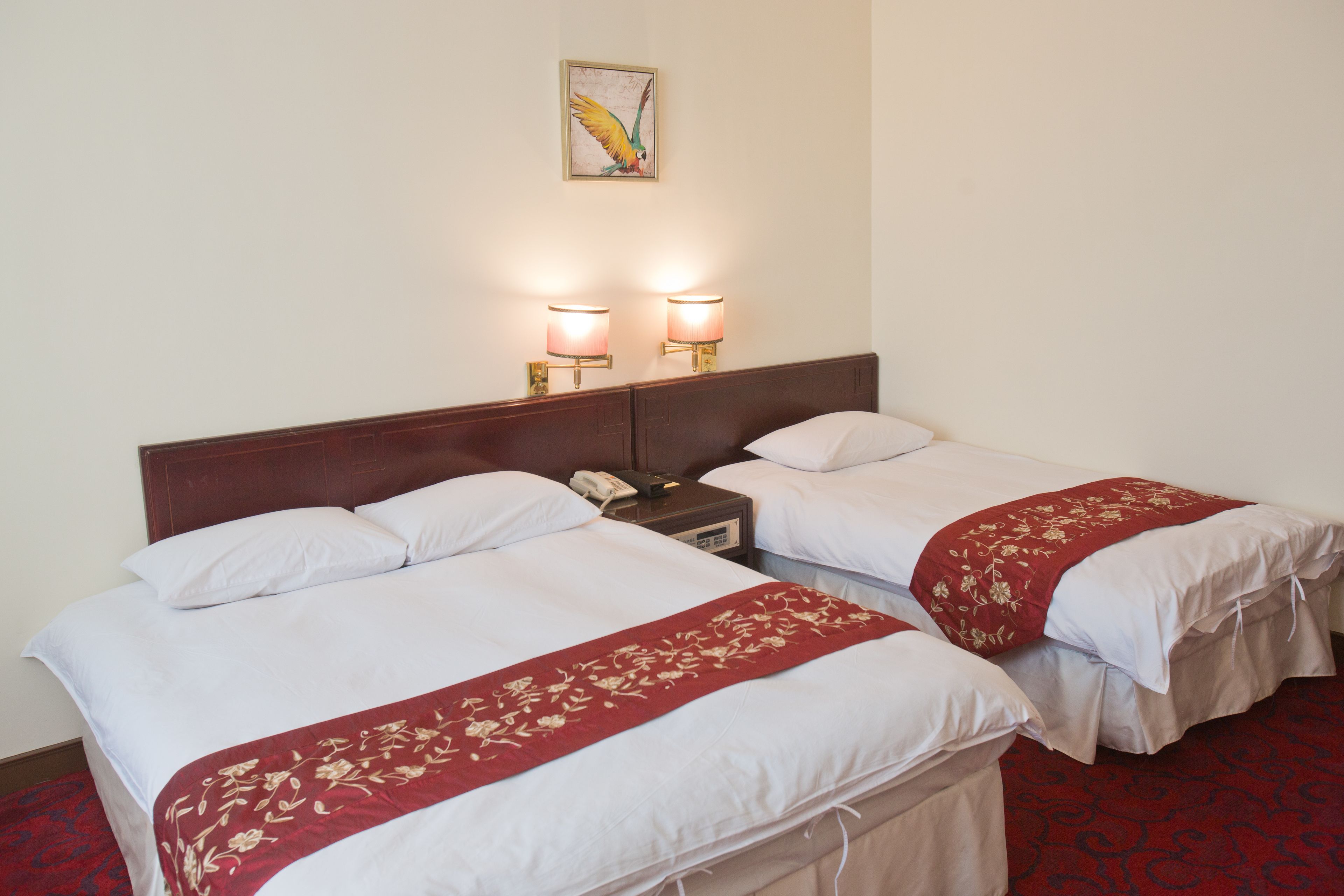 A hotel room with two beds, each with white linens and red floral bedspreads. There are two bedside lamps and a telephone on the nightstand.