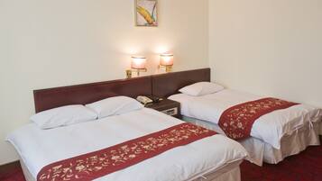 A hotel room with two beds, each with white linens and red floral bedspreads. There are two bedside lamps and a telephone on the nightstand.