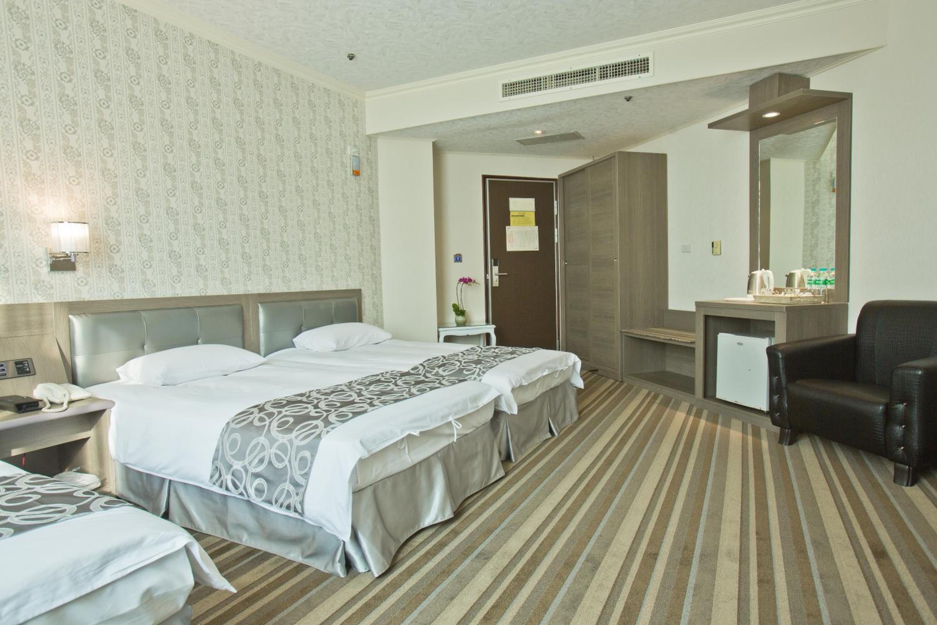 A hotel room with two beds, a desk, a chair, a mirror, and a small refrigerator.