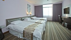 Una habitación de hotel con tres camas, un escritorio, un televisor y una ventana con cortinas.