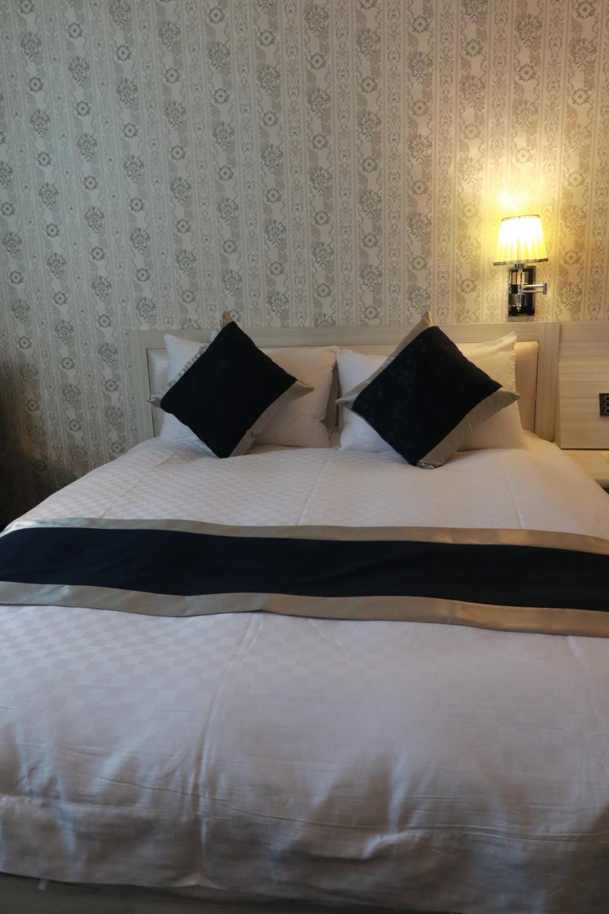 A neatly made bed with a white and black bedspread, two black pillows, and a wall-mounted lamp.