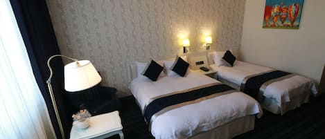 A hotel room with two beds, a desk, a lamp, and a painting on the wall.