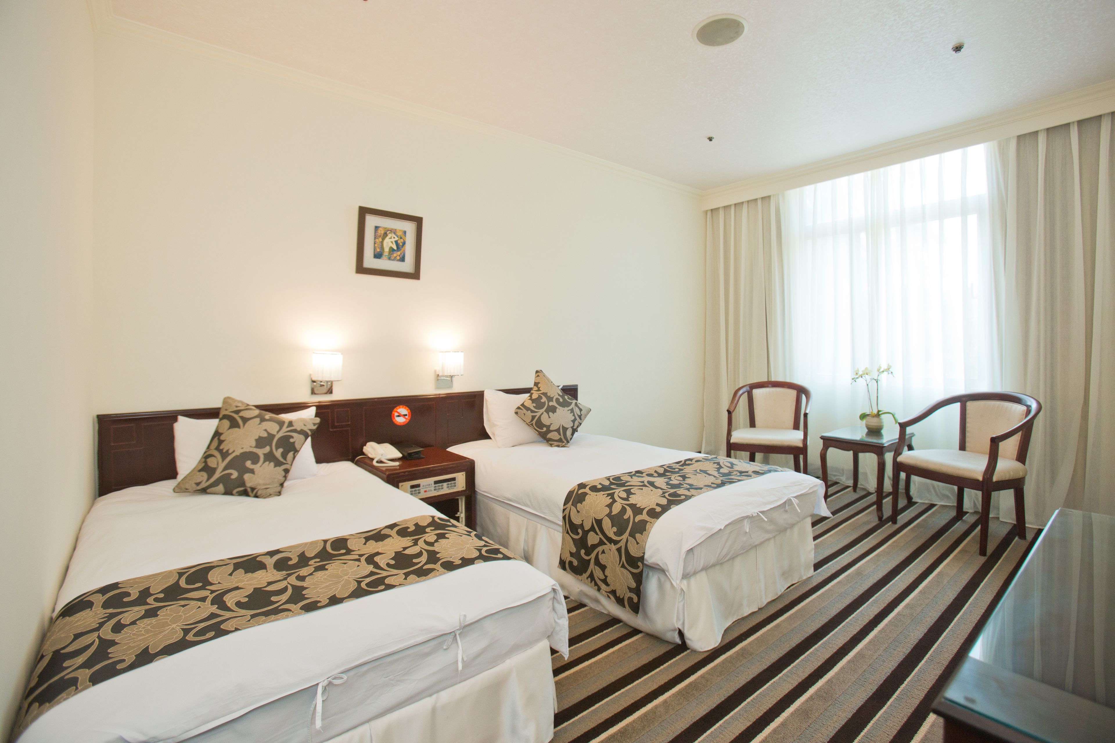 A hotel room with two beds, a desk, a chair, and a window with curtains.