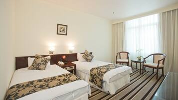 A hotel room with two beds, a desk, a chair, and a window with curtains.