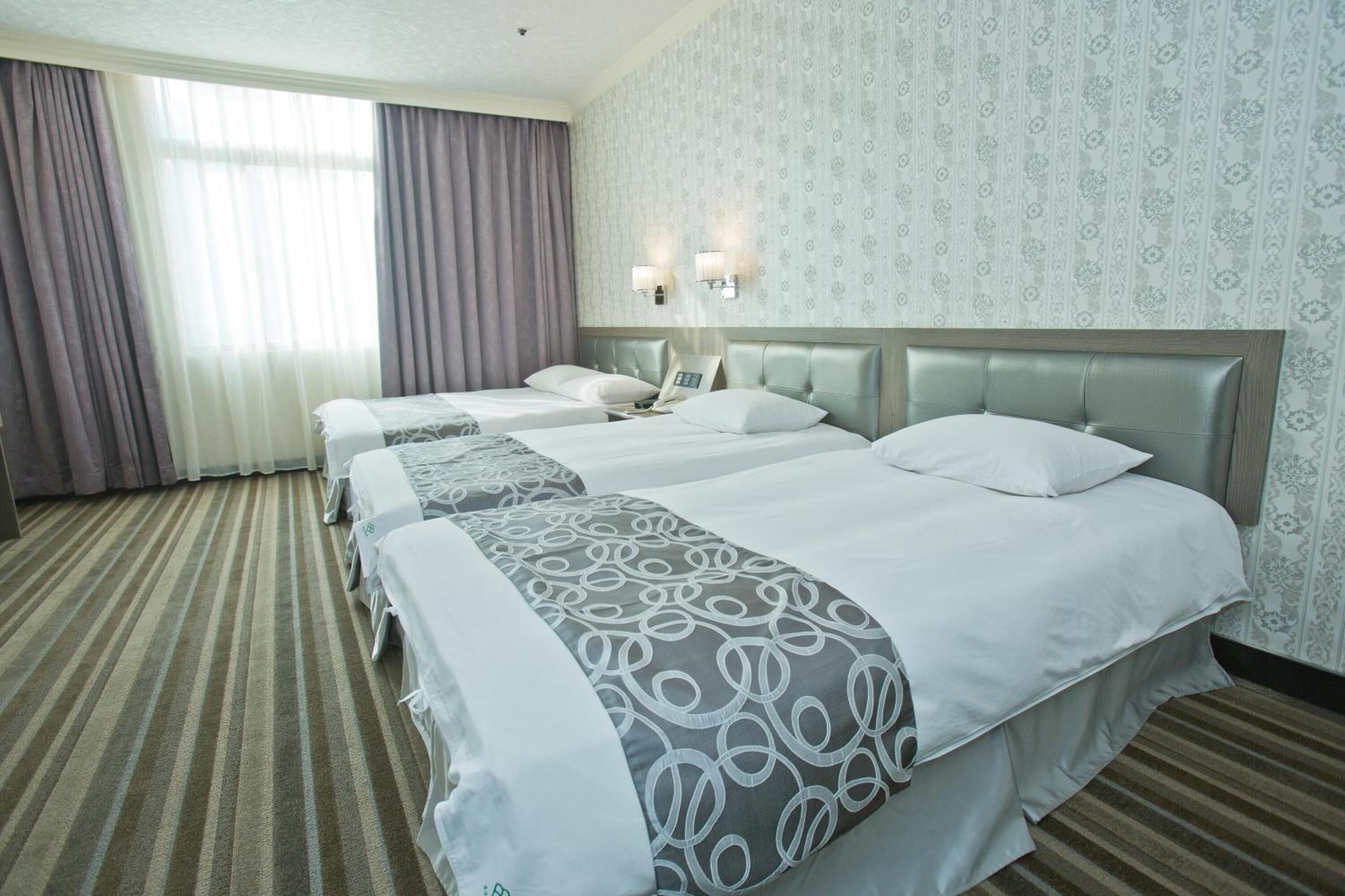 A hotel room with three beds, a striped carpet, and patterned wallpaper.