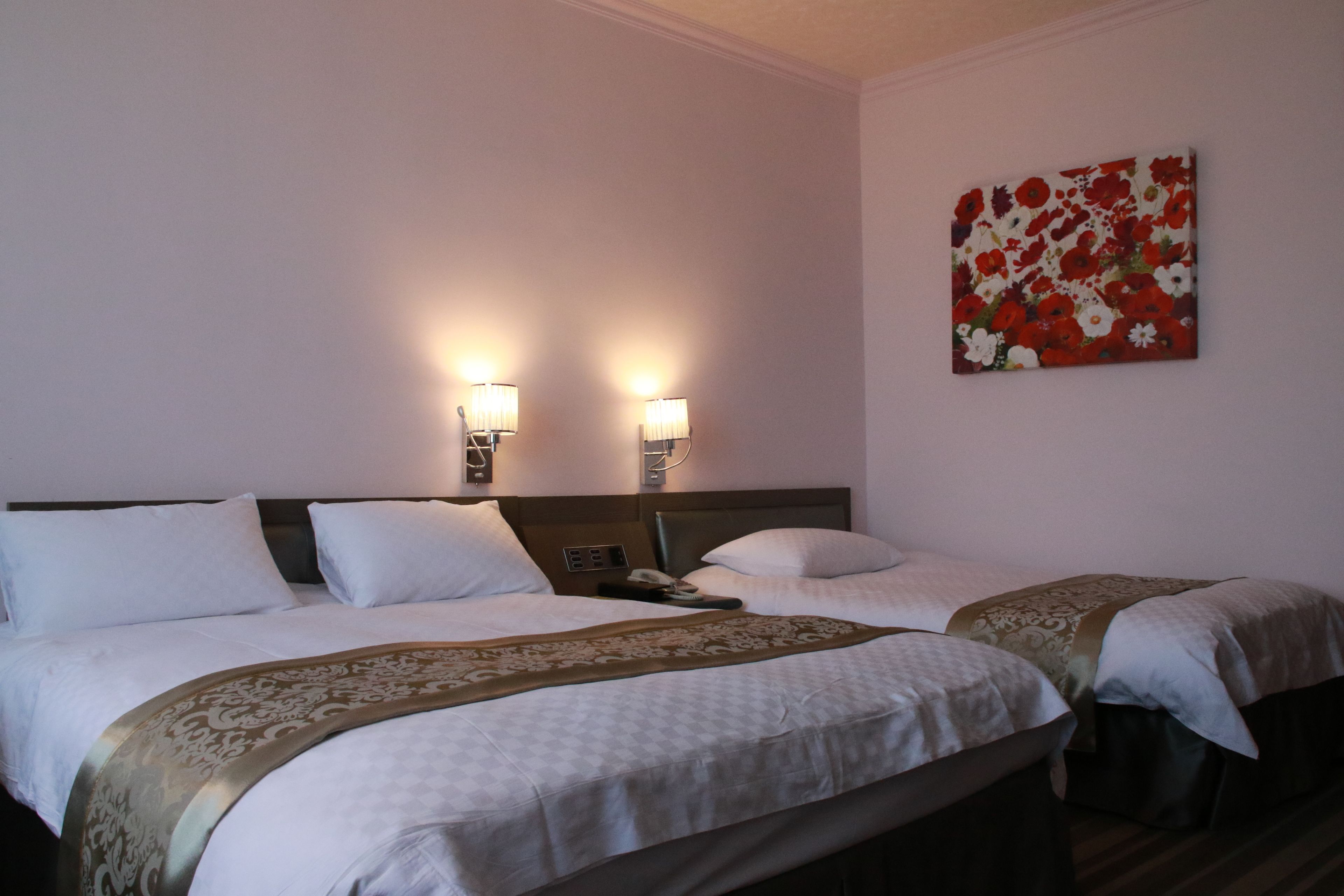 Une chambre d’hôtel avec deux lits, une table de chevet, un téléphone et deux lampes fixées au mur.