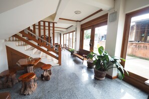 A spacious indoor area with a wooden staircase, a bench, and several potted plants. - Fah Place Hotel (Nan)