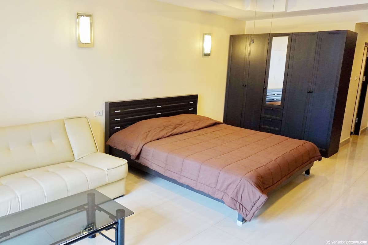 A bedroom with a bed, a white sofa, a glass coffee table, and a wardrobe.