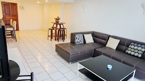 A living room with a dark brown leather sofa, a black coffee table, and a small round table with chairs. - Yensabai Condotel (Pattaya)