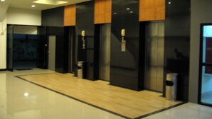 Un'area ascensore moderna con porte in vetro, pavimento in legno e cestino metallico.