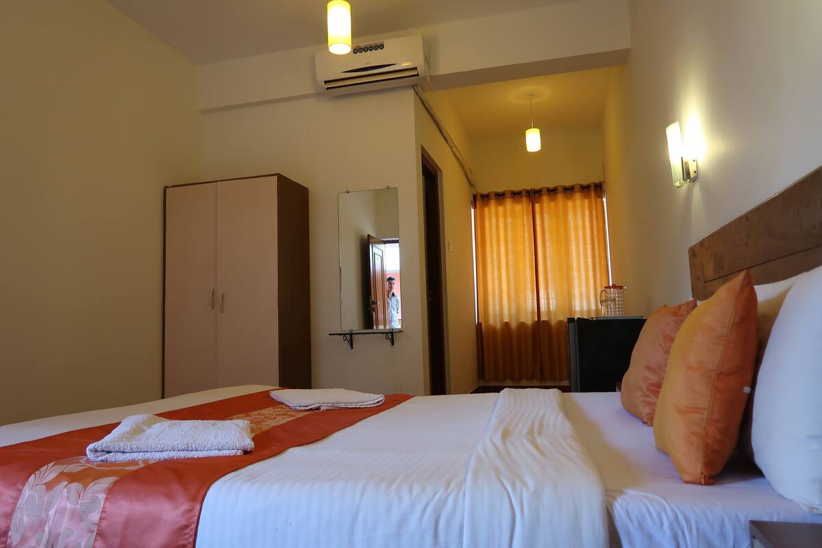 A hotel room with a bed, a wardrobe, a mirror, and a nightstand with a lamp.