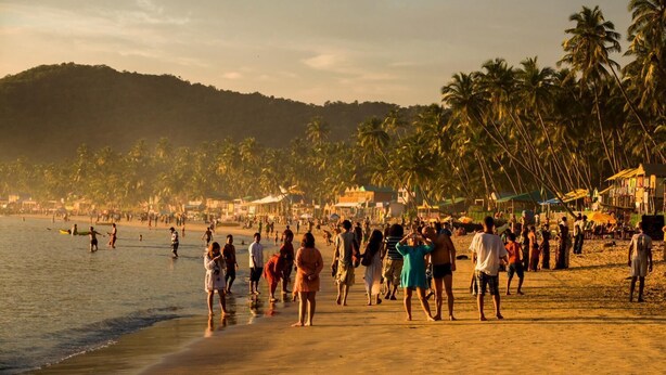 Una playa concurrida con palmeras y edificios al fondo.