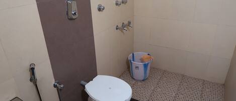 A small bathroom with a toilet, a shower, and a trash bin.