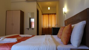 Habitación de hotel con cama, armario, espejo, mesita de noche y ventana con cortinas.