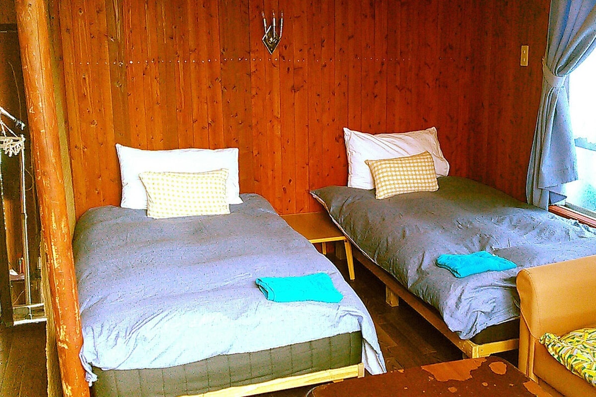 Une pièce avec deux lits, un mur en bois, une fenêtre et une chaise.