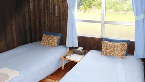 Ein Zimmer mit zwei Betten, einem kleinen Tisch mit Fernbedienung und einem Fenster mit Vorhängen.