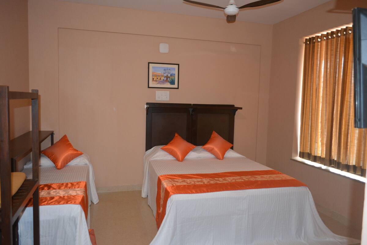 A hotel room with two single beds, a ceiling fan, a window with curtains, and a framed picture on the wall.