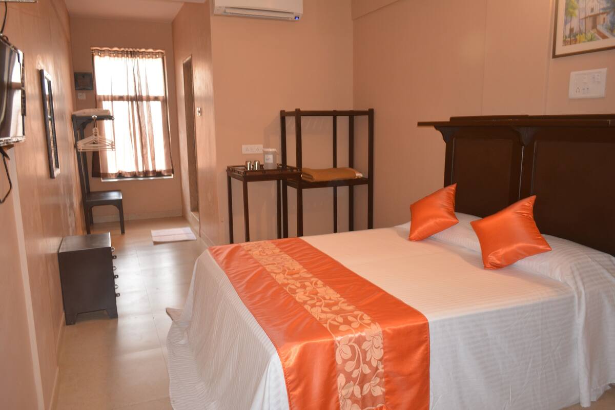 A hotel room with a bed, a chair, a small table, and a window with curtains.